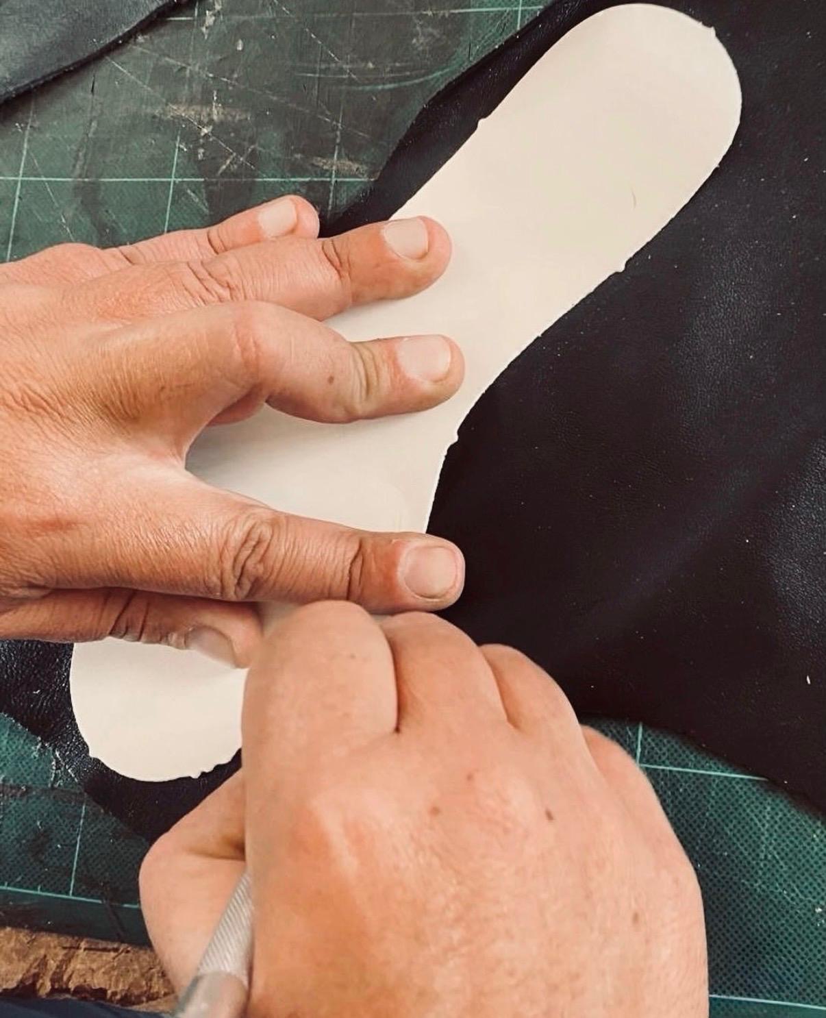 Artigiano che taglia a mano il sottopiede in pelle in un atelier toscano